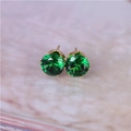 Macro view of 8mm green zircon stud earrings with gold six-claw setting on marble - Gold & Green