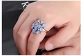 Gros plan d'une bague dorée réglable ornée de délicates fleurs bleu clair et de cristaux - Bleu