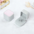 Nahaufnahme einer luxuriösen hellgrauen und rosa Samt-Ringbox auf weißem Kunstpelz - Rosa-Grau