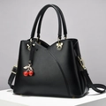 Elegant black leather handbag with red cherry charms and gold hardware on white pedestal - Black