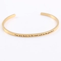 Macro shot of gold stainless steel bracelet with engraved inspirational quote text - You are born to be real not to be perfect