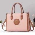 Detalle del bolso de cuero rosa y marrón con emblema dorado sobre una mesa blanca - Rosa
