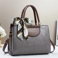 Detalle de bolso gris con textura geométrica, asas marrones y un pañuelo decorativo elegante - Gris