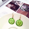 Detail of cucumber slice drop earrings with green enamel hanging on a white porcelain bowl - Cucumber