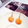 Creative orange slice drop earrings with golden hooks shown on a white ceramic tray - Orange