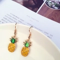 Dettaglio degli orecchini a forma di ananas giallo e verde appesi a una tazza bianca - Ananas