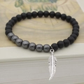 Pulsera de cuentas negras mates y hematita con colgante de hoja plateada sobre libro antiguo - Colgante de Pluma Plateada / Plateado