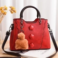 Dettaglio borsa rossa in ecopelle con fiori 3D e portachiavi a pompon marrone lucido - Rosso Vino