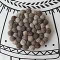 Macro shot of handmade round wool felt ball coaster in dark brown and beige tones - Gray