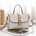 Elegante borsa in pelle crema con cinturino grigio e finiture dorate su fondo di legno - Bianco Sporco