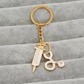 Macro shot of gold medical keychain with white enamel syringe and stethoscope details - Gold