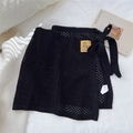 Détail d'une jupe portefeuille en maille noire avec nœud latéral et étiquette jaune - Taille unique / Noir
