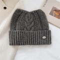 Close-up of dark grey wool knit beanie showing thick cable pattern and metal logo detail - 24*20cm / Gray