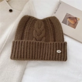 Détail du bonnet en grosse maille torsadée montrant la texture et l'écusson métallique - Marron