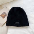 Detalle del gorro de punto de felpa negro con etiqueta BOWLOW sobre fondo de tela blanca - 24*23cm / Negro