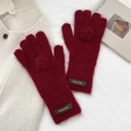 Detail of dark red knit gloves with soft fur pompom and leather logo label - Gloves / Burgundy
