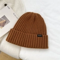 Detailed view of brown wool knit beanie texture with a woven patch on a white background - One Size / Orange