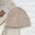 Detailed view of beige ribbed knit beanie featuring a metallic logo tag and soft texture - Off White
