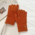 Close-up of warm orange knitted gloves featuring a leather brand tag and ribbed cuffs - One Size / Orange