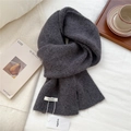 Detail of soft dark grey wool knit scarf with brand label on a cozy white bed - Black and Gray