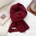 Close-up of a soft burgundy wool knit scarf featuring textured weave and white brand label - Burgundy