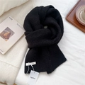 Detail shot of a black wool knit scarf showing its soft texture and white brand label - Black