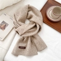 Detail of oatmeal ribbed knit scarf with a small brown leather tag on soft white bedding - 26*180cm / Beige Coffee