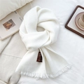 Close-up of white knit scarf with fringe detail and wool label on soft fabric background - White