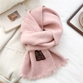Detail of soft light pink knitted wool scarf featuring fringe edges and woven tag - Pink