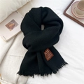 Close-up of black knitted winter scarf with tassels and stitched label on white fabric - Black