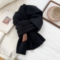 Detailed close-up of a black ribbed knit scarf with a handmade leather patch label - Black