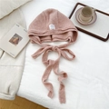 Detailed knit texture of pink hooded beanie with ribbon ties on white bedding - Pink