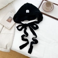 Detail of black knit balaclava with decorative label and long straps on white bedding - Black