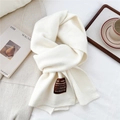 Detail of soft off-white knit wool scarf with ribbed edges and label on white bedding - One Size / Heathered Milk White