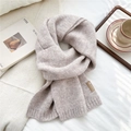 Detail of oatmeal knit scarf showing ribbed texture and leather tag on a bed - White Coffee