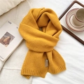 Detailed close-up of a warm yellow knitted scarf featuring a brown leather brand tag - Yellow