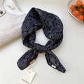 Carré de soie à motif paisley noir et blanc noué avec étiquette de marque visible - Paisley Résille Noir