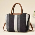 Close-up of tricolor woven striped handbag with brown leather handles and metal hardware - Black