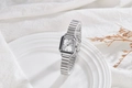 Detail view of a square silver quartz watch with a minimalist Roman numeral dial and band - White