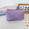 Close-up of a purple quilted heart pattern cosmetic bag with a zipper on a desk - Quilted Heart Purple