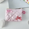 Detailed view of pink quilted lipstick bag with bow accents on a desk setup - Pink