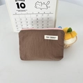 Dettaglio della pochette in nylon a quadretti con bordo rosa e zip blu sul tavolo - Marrone