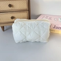 Close-up of white quilted makeup bag with silver ring zipper on vintage wooden desk - Quilted Diamond White