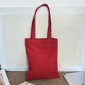 Minimalist red canvas tote bag shown with a tablet on a brown woven mat backdrop - 8oz / Red