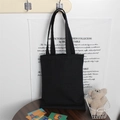 Detailed view of the thick black cotton canvas tote bag hanging on a hook in a cozy setting - Black (12oz)