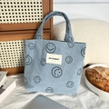 Close-up of light blue corduroy tote bag with black smiley faces and May Rabbit woven label - Light Blue Gray Smiley Face