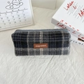 Close-up of a grey plaid wool pencil case with a brown leather tag on a desk - Woolen Dark Gray Beige Plaid