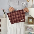 Cartera de mano de lona a cuadros marrones y beige sostenida en un ambiente minimalista - Cuadros Rojo Vino