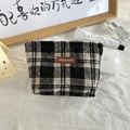Macro-opname van zwart-wit geblokte tweed make-up tas met een lederen label op een bureau - Wollen Zwart Wit Geruit
