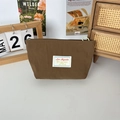 Detail view of coffee-colored fabric makeup bag with green zipper and branded fabric label - Brown